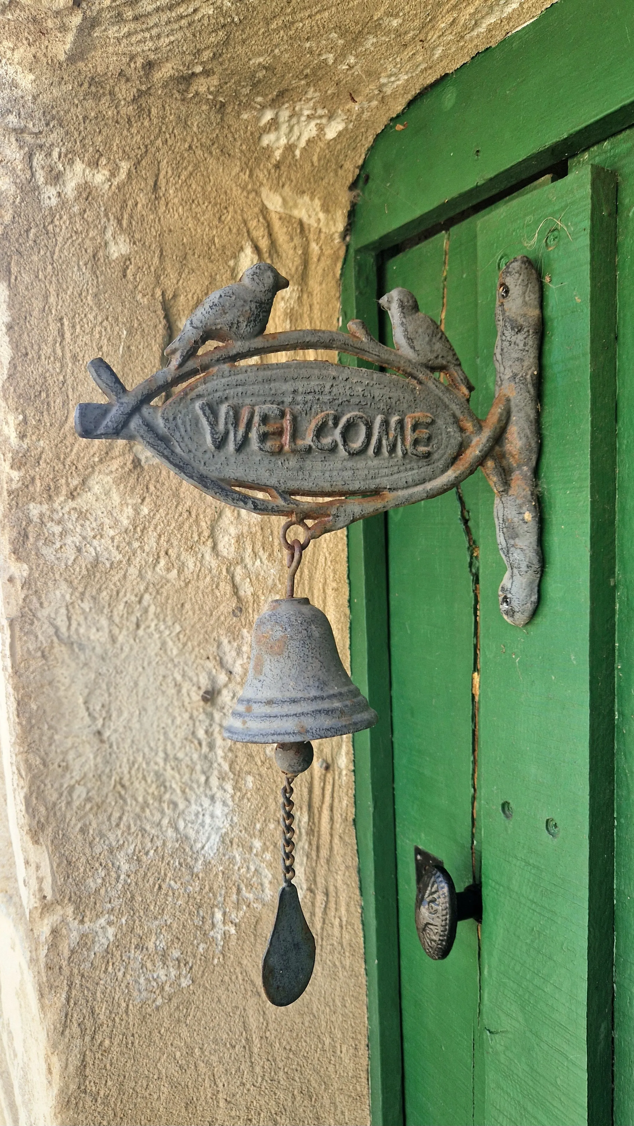 Cloche « Welcome » en fonte près de la porte verte