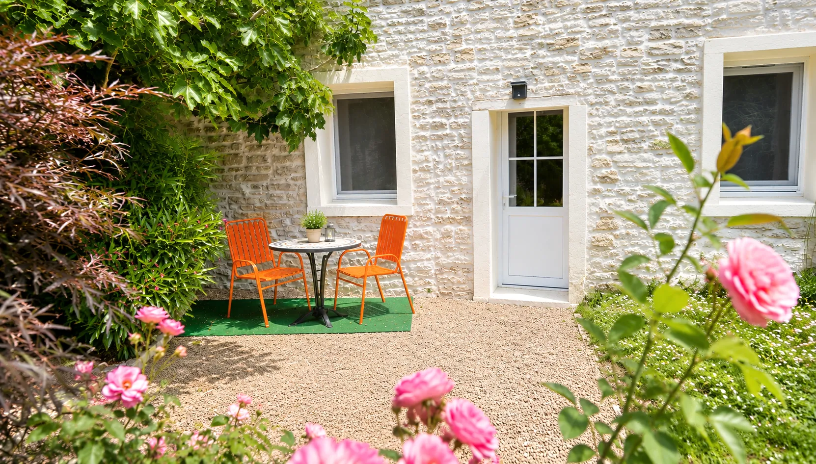 Terrasse et façade en pierre du gîte, jardin fleuri de roses